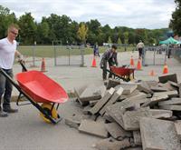 At a school depave event, two individuals unload red wheelbarrows contributing to the removal of hard surfaces on the school property. A substantial pile of removed material is visible.