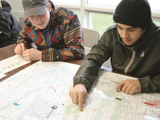 Two students look at a map in a classroom. One student points to a location on the map as the other smiles in agreement.