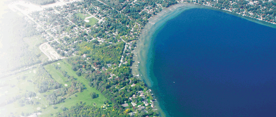 An aerial photo of Lake Simcoe. The Lake is surrounded by forests and urban neighbourhoods.