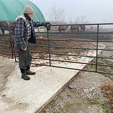 Mike Lanigan stands on a concrete pad near a clean water diversion system and a fenced area housing his cattle.