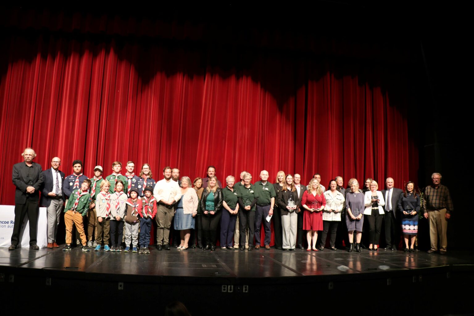 All of the 2023 conservation award recipients standing side by side on the stage with a red curtain behind them.